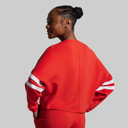 Person wearing a red sweatshirt with white stripes on sleeves against a gray background