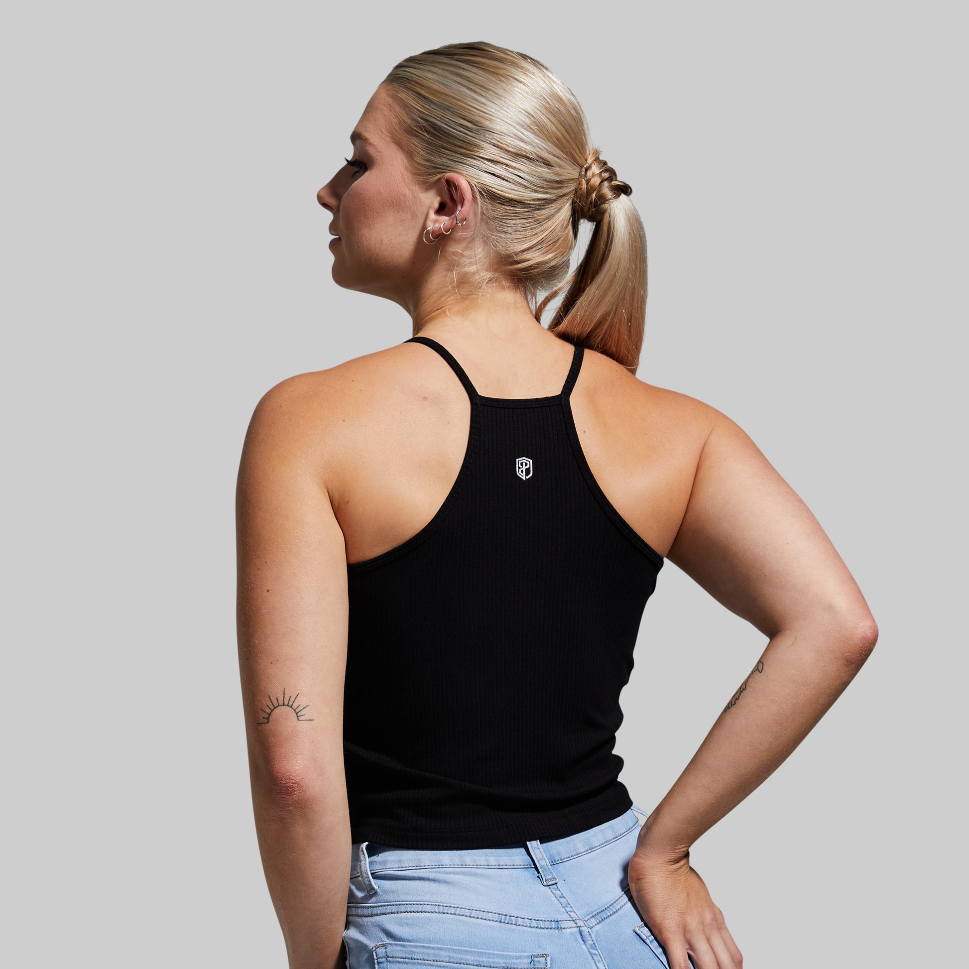 Woman wearing a black tank top with a small logo on a gray background