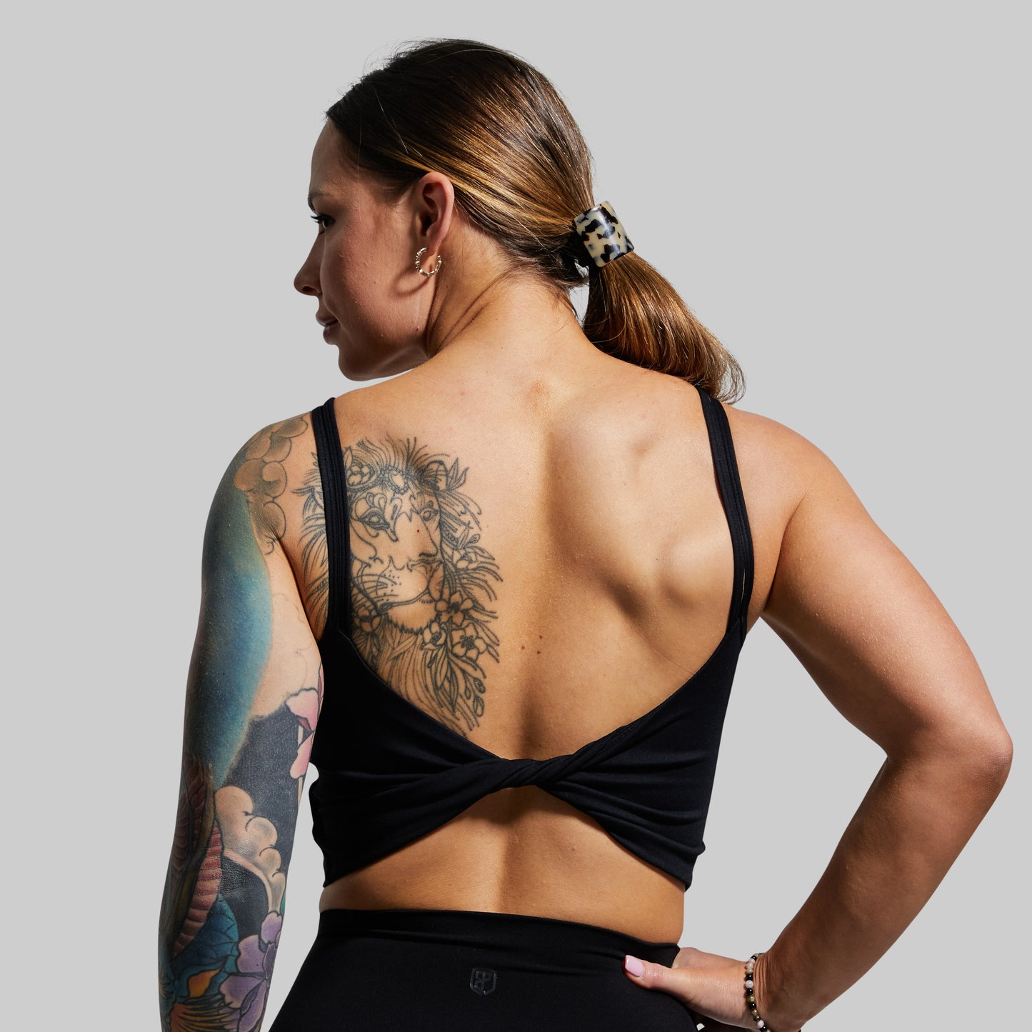 A woman is shown from the back wearing a black sports bra with a twisted design at the back.