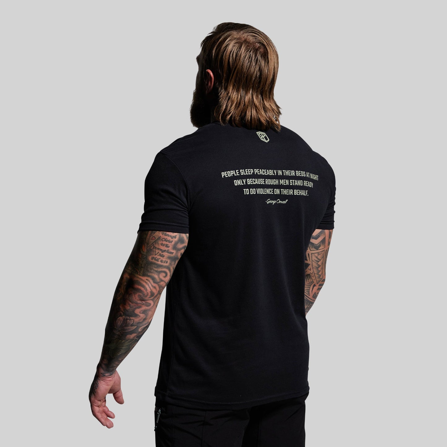 Person wearing a black t-shirt with text on the back, standing against a plain background