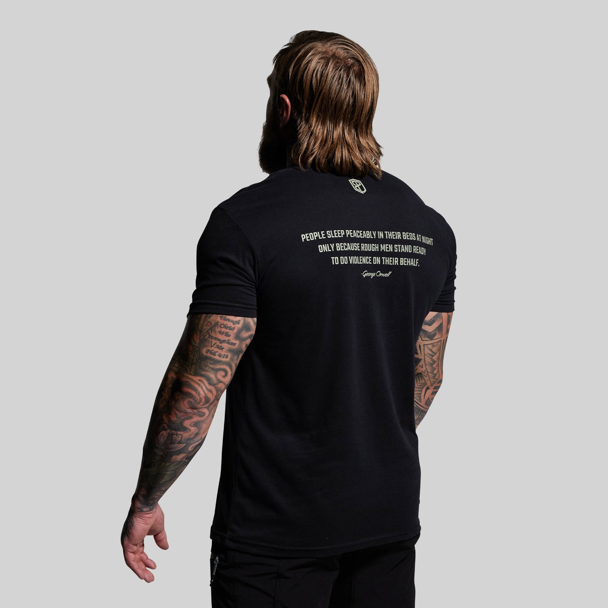 Person wearing a black t-shirt with text on the back, standing against a plain background