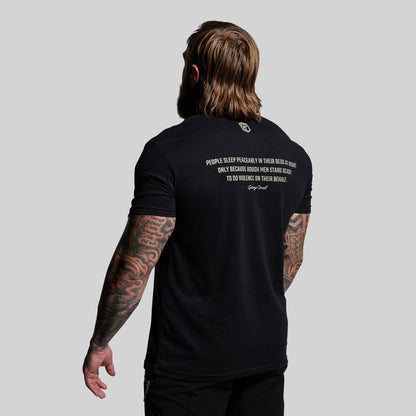 Person wearing a black t-shirt with text on the back, standing against a plain background