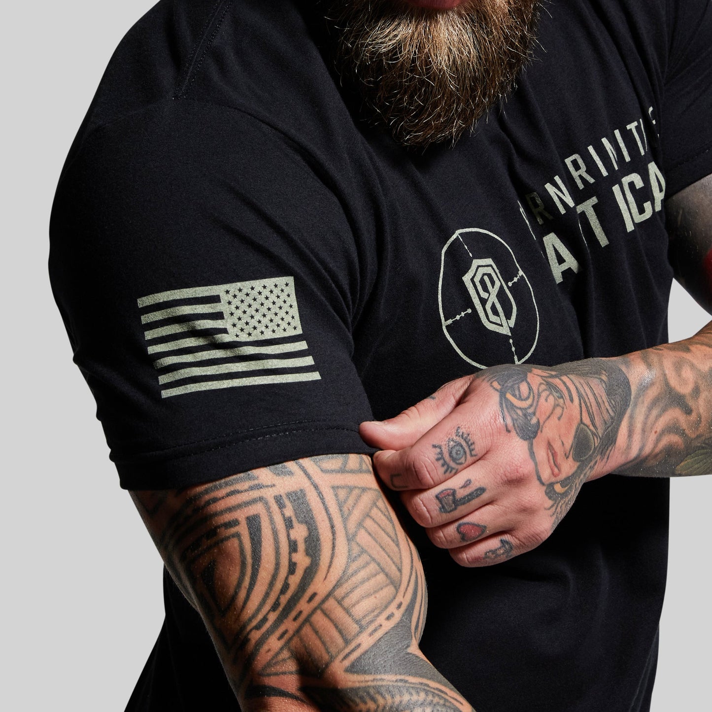 Person wearing a black t-shirt with an American flag patch and tattoos on arms.