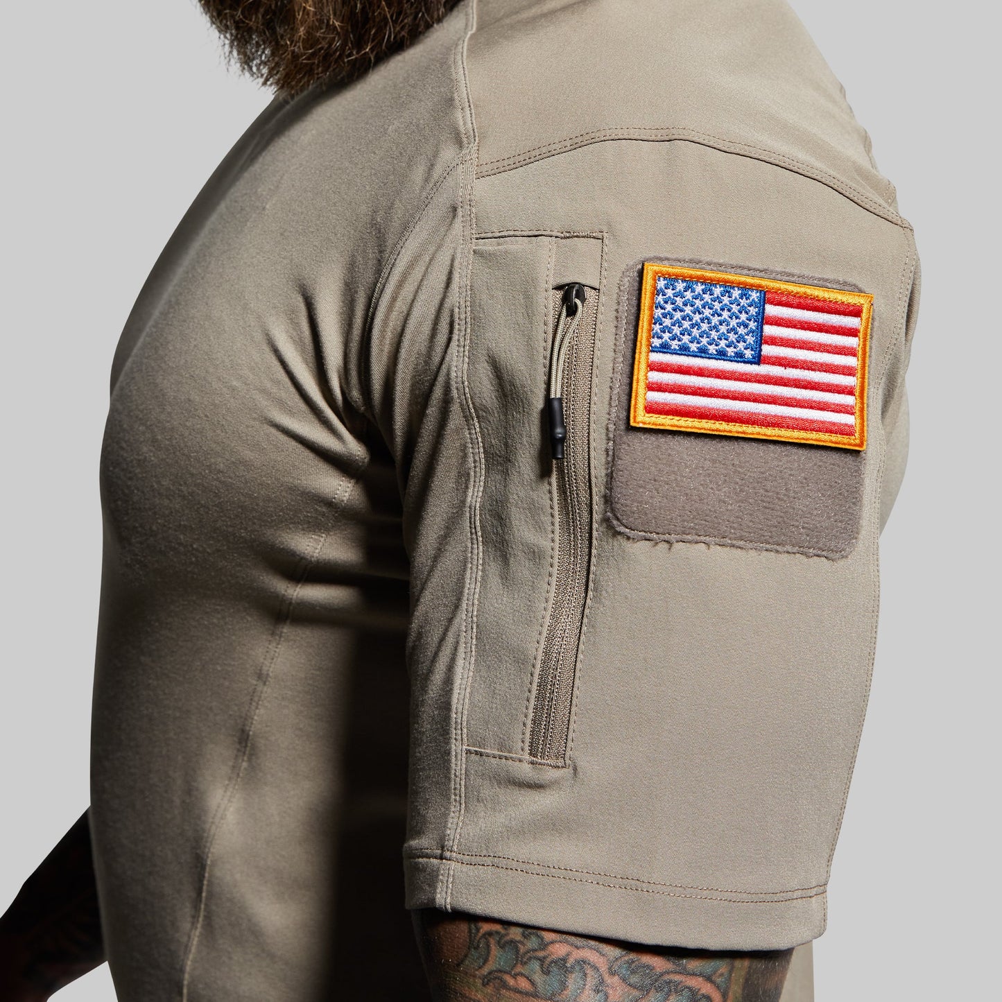 Person wearing a beige shirt with an American flag patch on a gray background