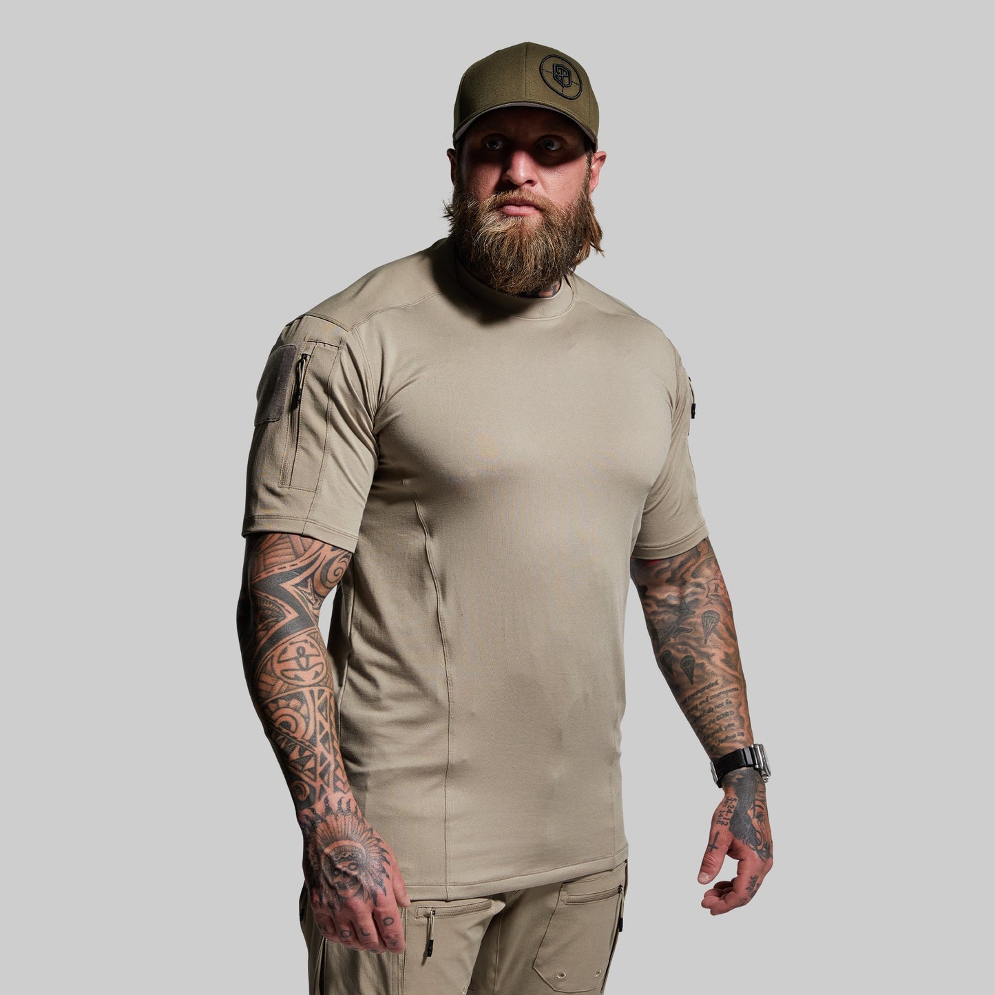 Man wearing a beige tactical outfit with a cap on a gray background