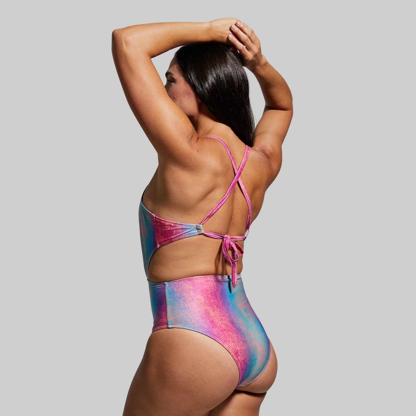 Woman wearing a colorful one-piece swimsuit with a strappy back design against a gray background