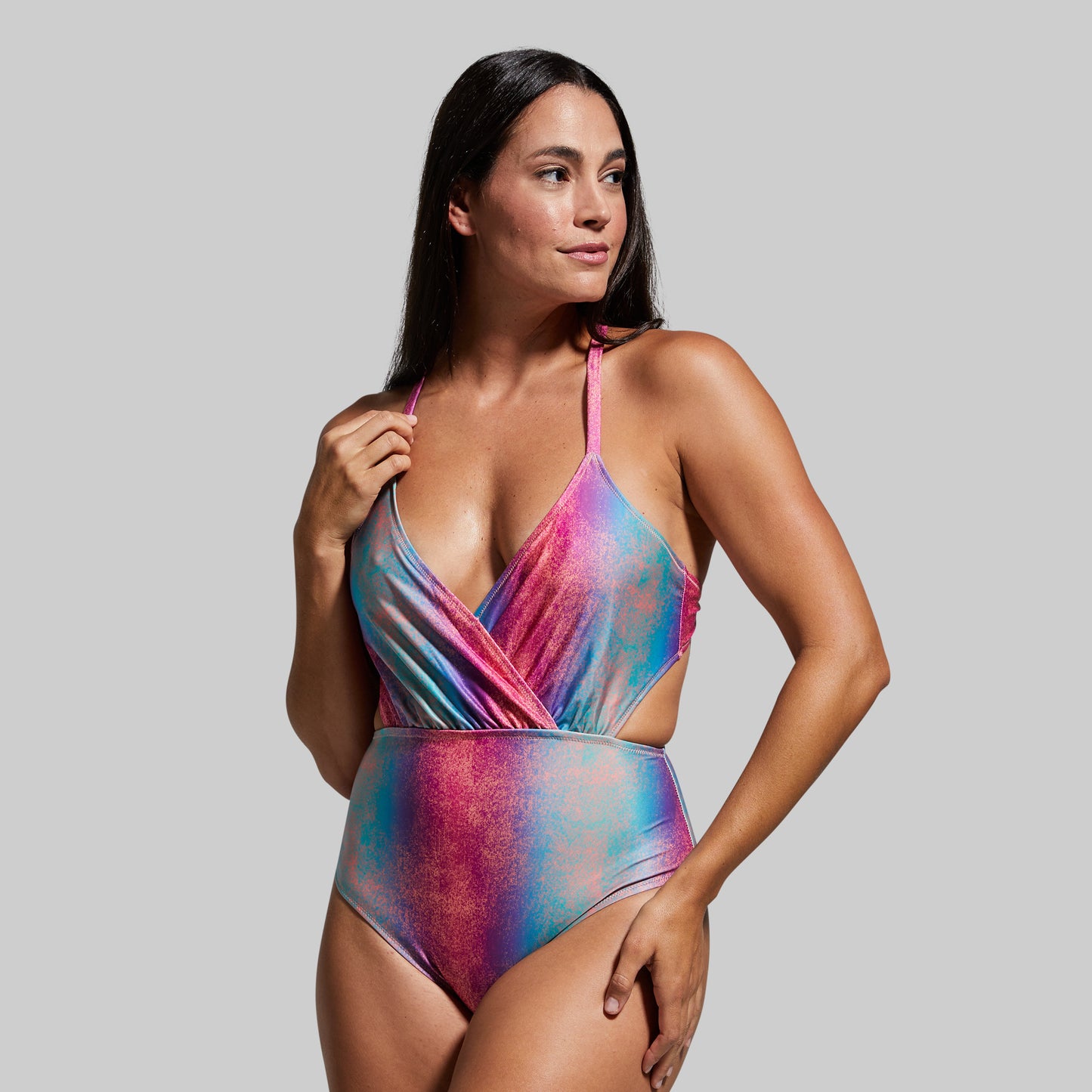 A woman wearing a fluorescent multicolor one-piece swimsuit with a crisscross front and compression-like midsection.