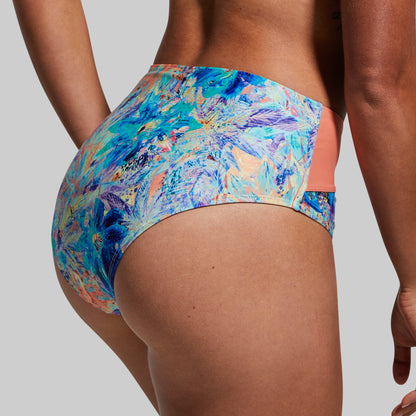 A rear view of a person wearing a multicolored floral bikini bottom with bright blue and flame design accents.