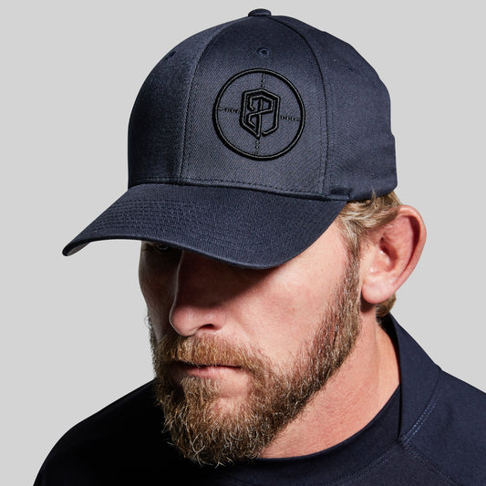 Man wearing a navy blue cap with a logo on a gray background