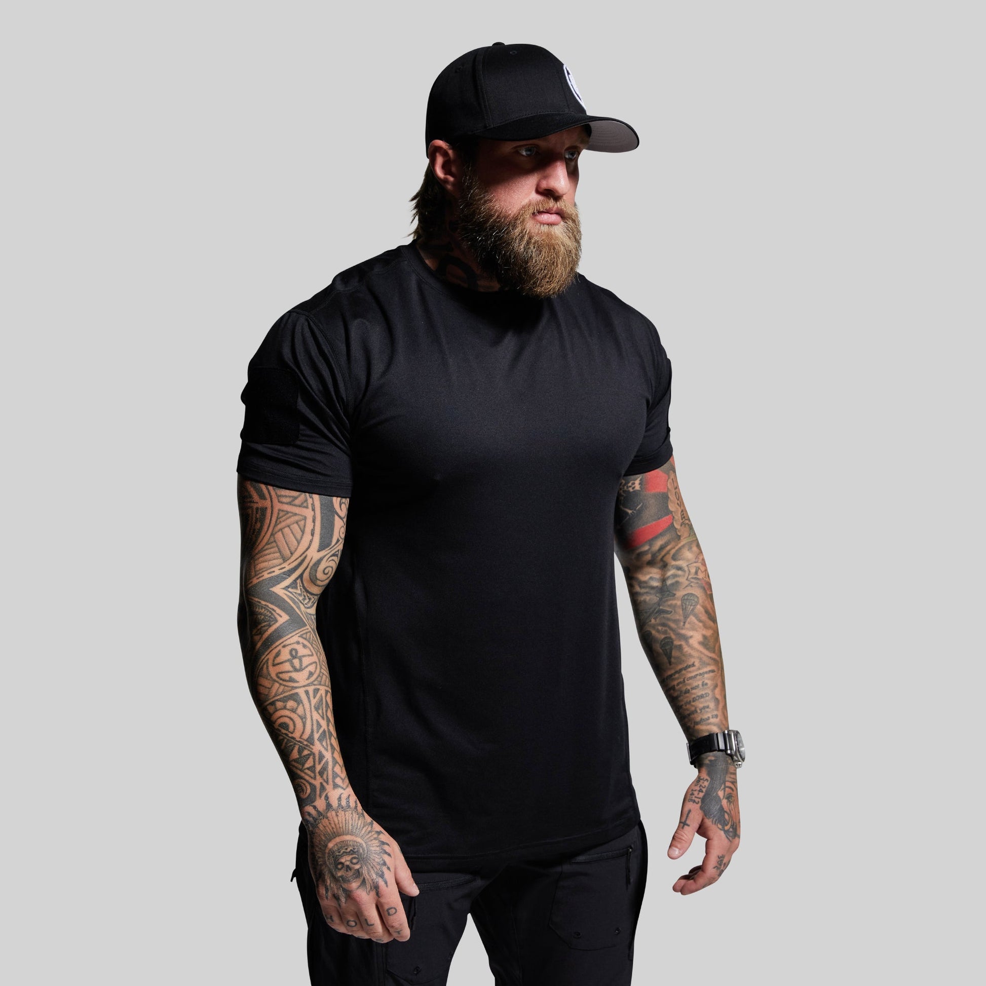 Man wearing a black t-shirt and cap with tattoos on arms against a gray background
