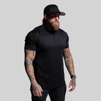 Man wearing a black t-shirt and cap with tattoos on arms against a gray background