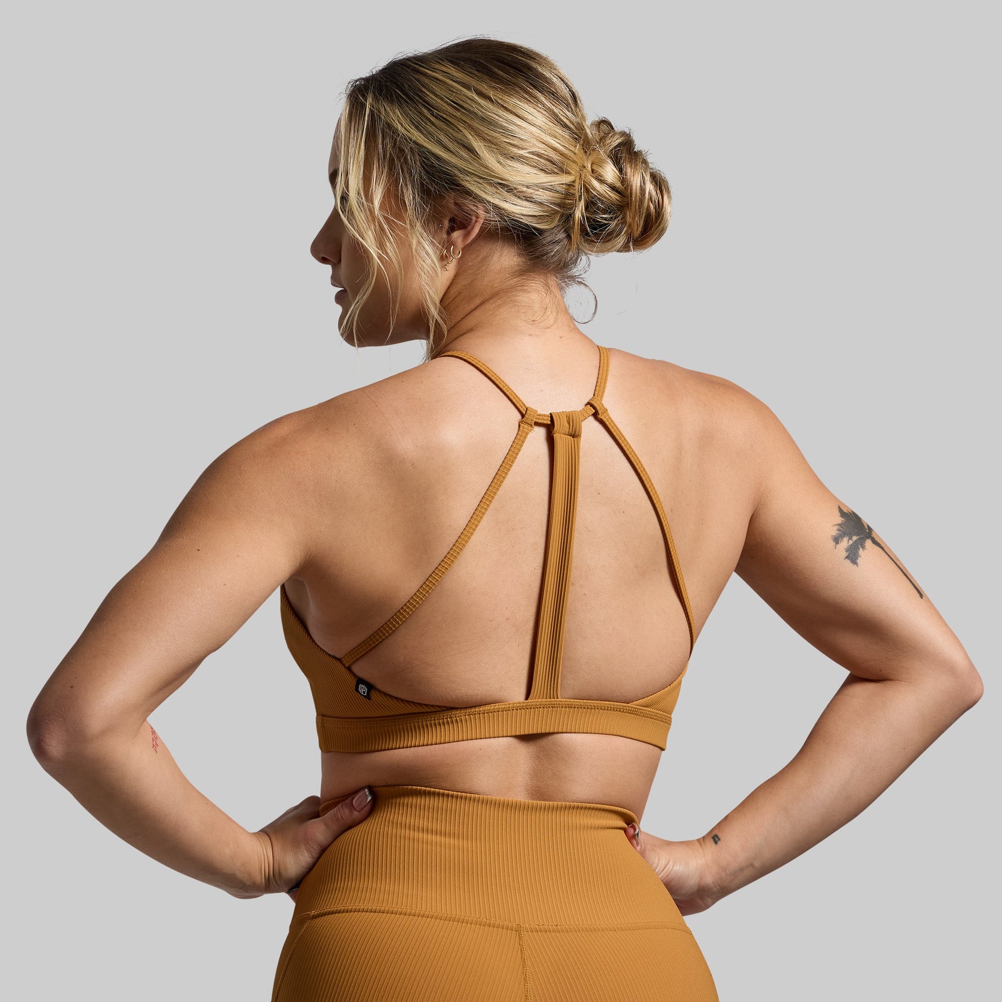 Woman wearing a mustard yellow sports bra and leggings on a gray background