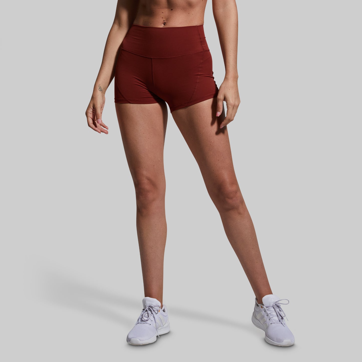 Person wearing maroon athletic shorts and white sneakers on a gray background
