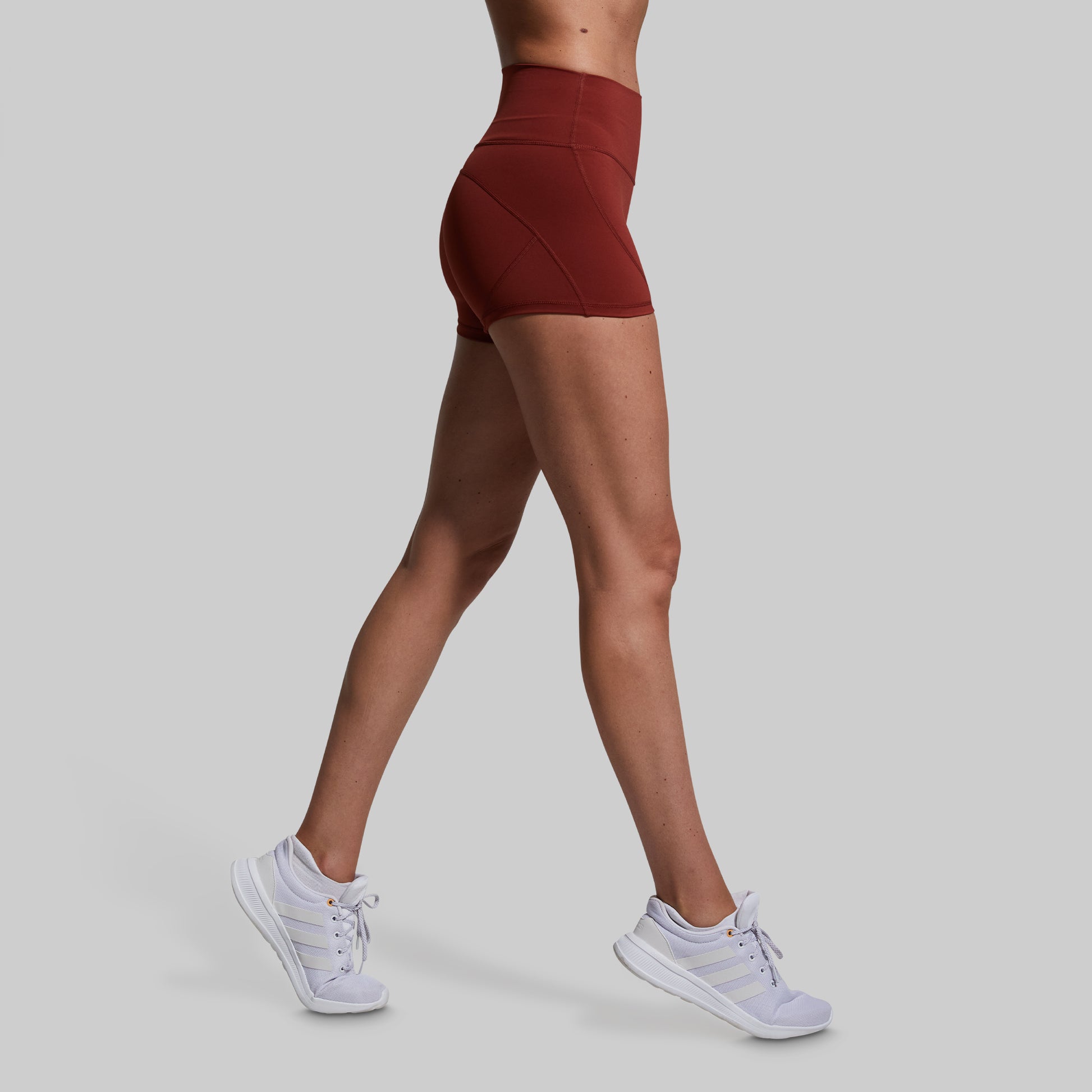 Person wearing maroon high-waisted shorts and white sneakers on a light gray background