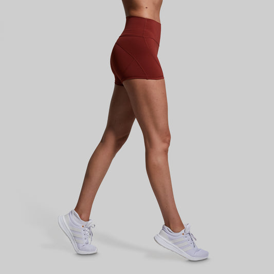 Person wearing maroon high-waisted shorts and white sneakers on a light gray background