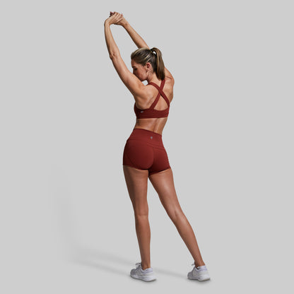 Woman in red athletic outfit stretching against a gray background