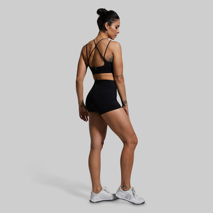 Woman wearing a black sports bra and shorts on a gray background
