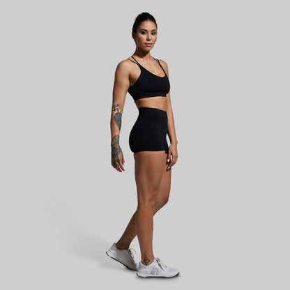 Woman wearing a black sports bra and shorts on a gray background