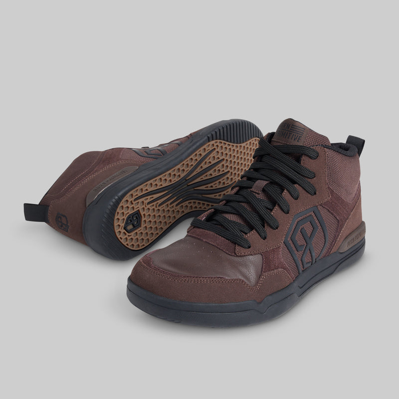 A pair of mid-top athletic sneakers in dark brown and black, with one shoe showing the side profile and the other showing the textured outsole, set against a solid gray background.
