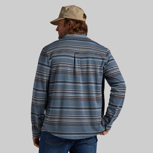 A man wearing a blue striped long-sleeve shirt and a tan baseball cap, photographed from the back against a solid gray background.