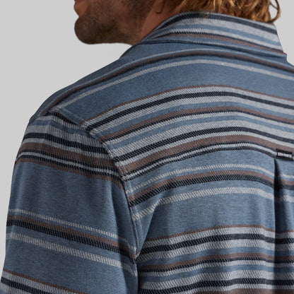 Close-up of a man wearing a blue striped knit shirt, showing the back of his neck, head, and shoulder against a light gray background.