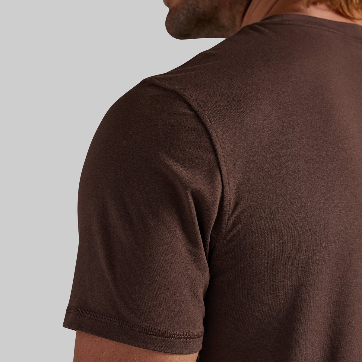 Close-up of a man wearing a dark brown short-sleeve crewneck t-shirt, showing the back and shoulder area against a light gray background.