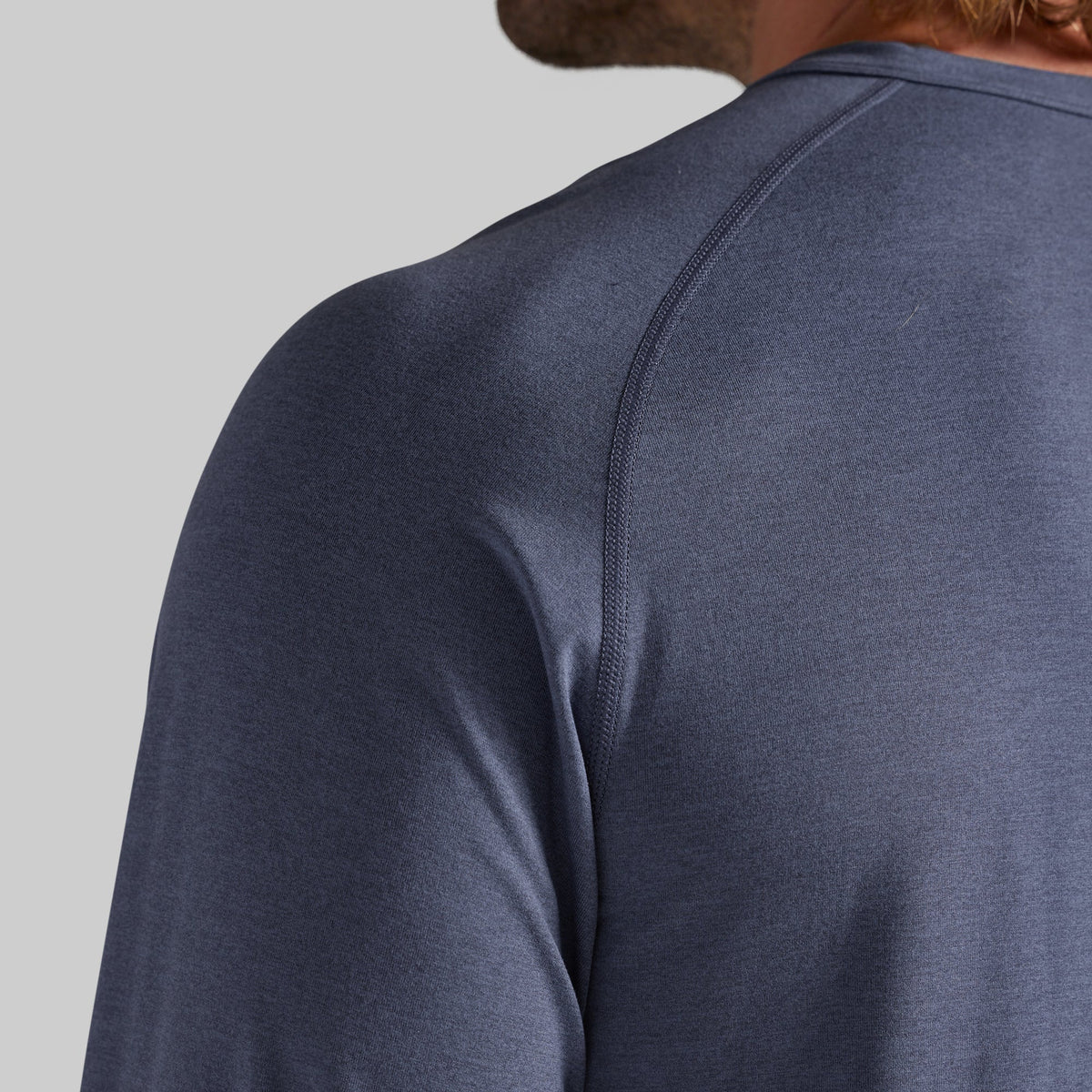 Close-up back view of a person wearing a heathered slate blue long-sleeve athletic shirt, showing the shoulder seam and neck area against a light gray background.