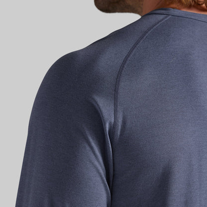 Close-up back view of a person wearing a heathered slate blue long-sleeve athletic shirt, showing the shoulder seam and neck area against a light gray background.