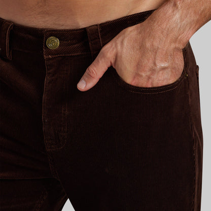 Close-up of a person wearing dark brown corduroy pants, with the hand tucked into the front pocket and a visible gold-tone button at the waistband.