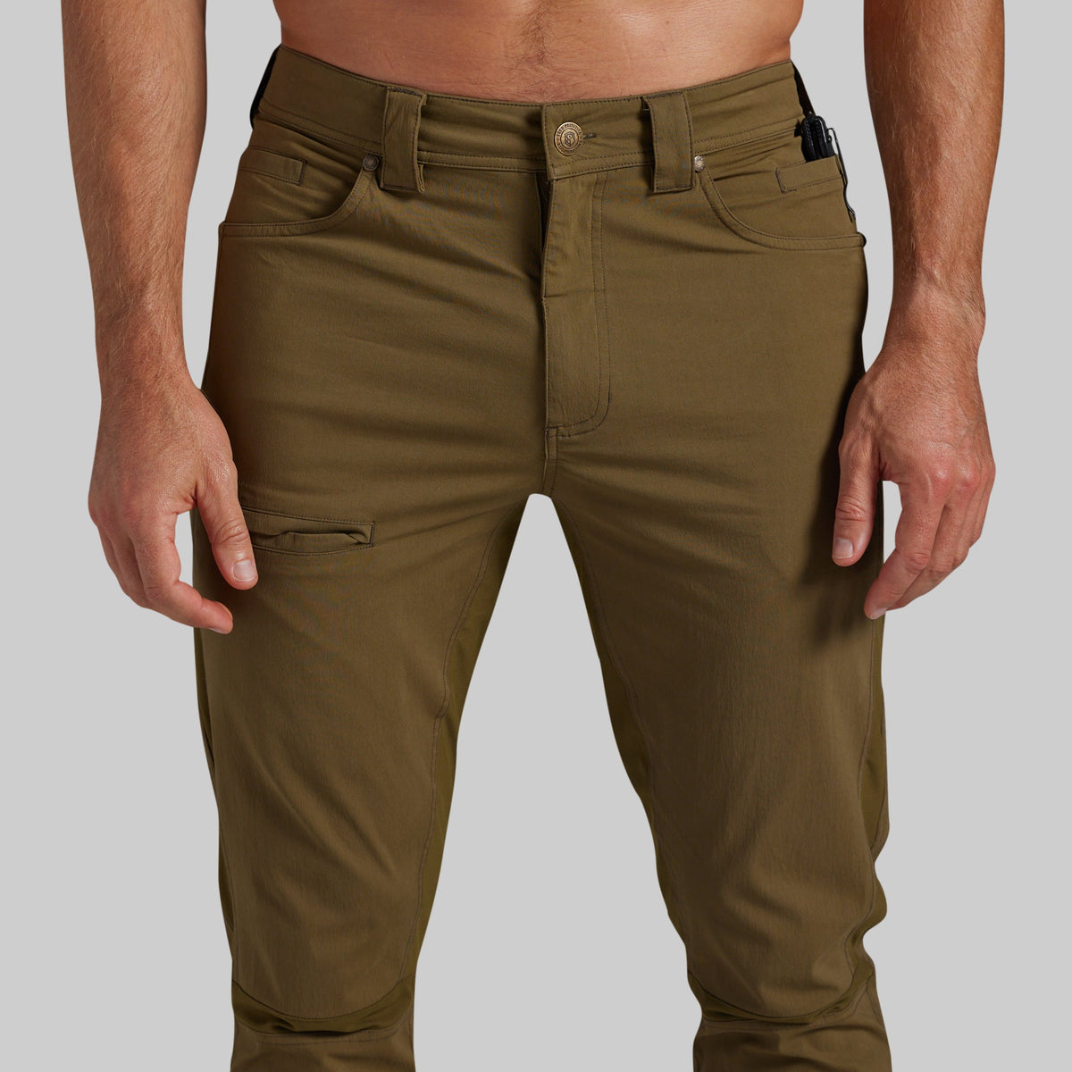 A close-up of a person wearing olive green cargo-style pants against a light gray studio background.
