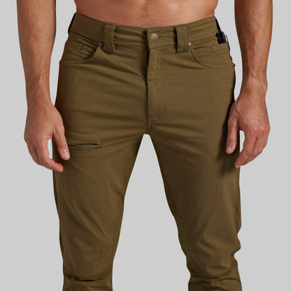 A close-up of a person wearing olive green cargo-style pants against a light gray studio background.