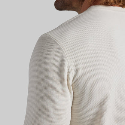 Close-up back view of a person wearing a textured off-white waffle-knit long-sleeve top against a light gray studio background.