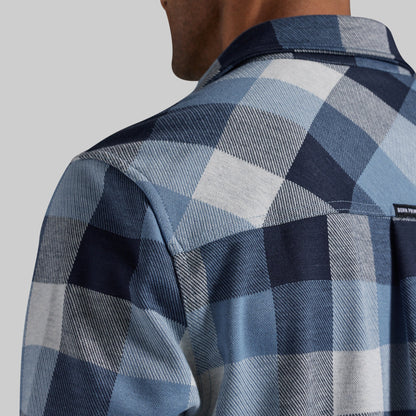 Close-up of a man wearing a blue and white plaid flannel shirt, showing the back of the neck, collar, and shoulder with a small visible brand tag.