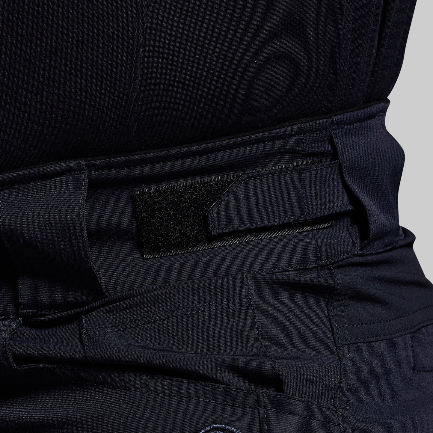 Close-up of blue tactical pants with an adjustable waistband on a gray background