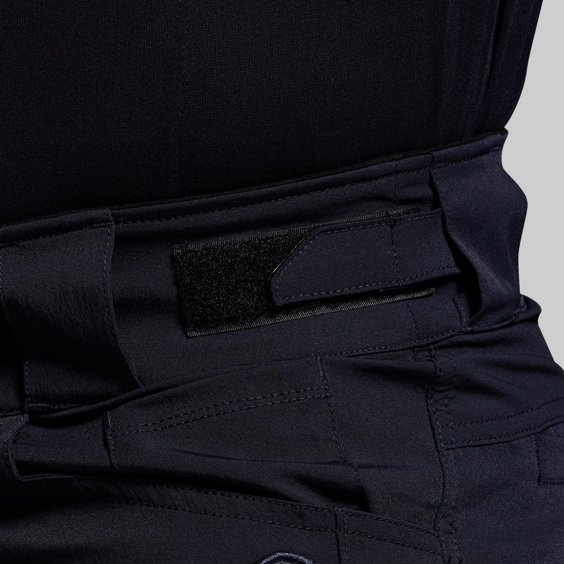 Close-up of blue tactical pants with an adjustable waistband on a gray background