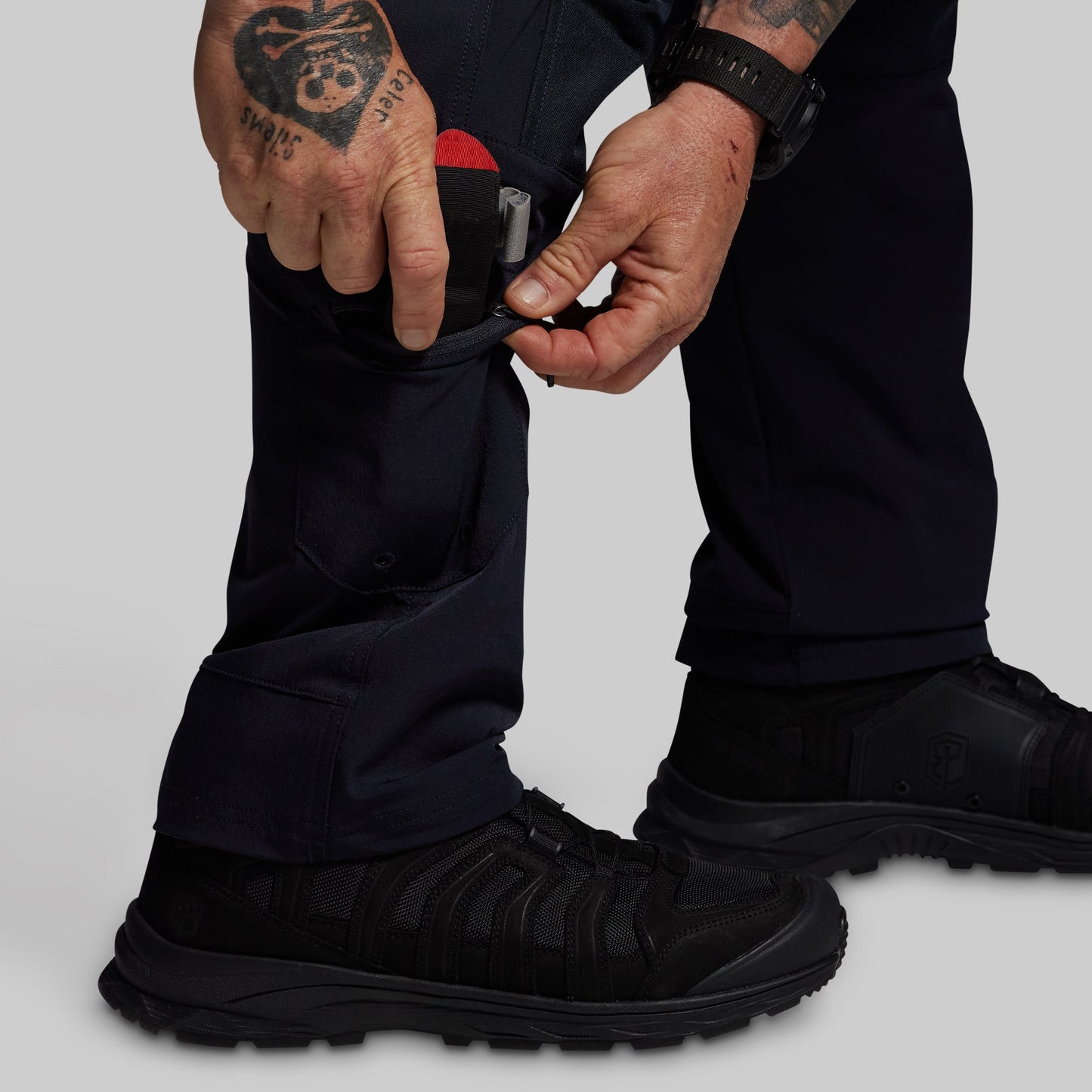 Person wearing black boots and blue pants with a tattooed hand adjusting a boot.