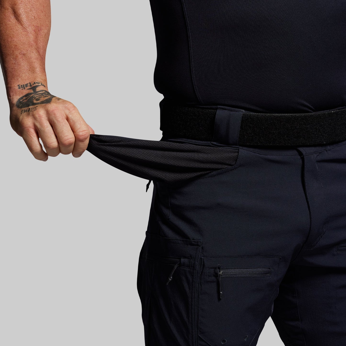 Person wearing blue pants with a tattoo on the arm against a gray background
