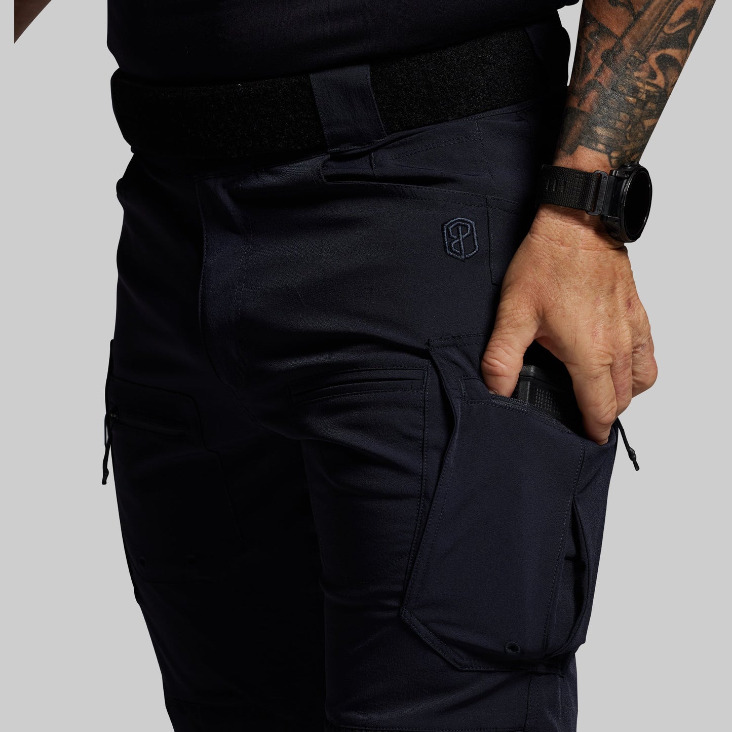 Person wearing blue tactical pants with a visible brand logo on a gray background
