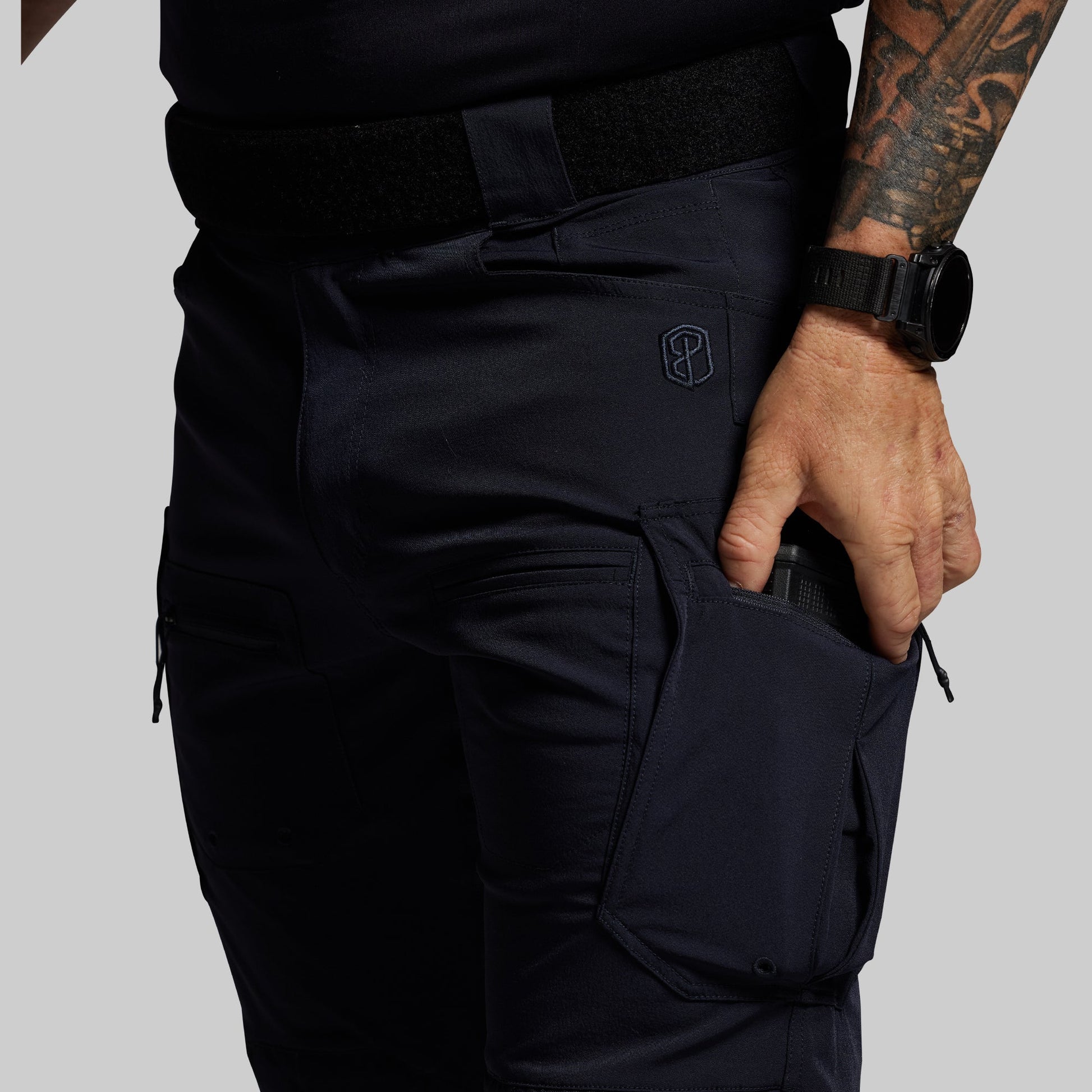 Person wearing blue tactical pants with a visible brand logo on a gray background