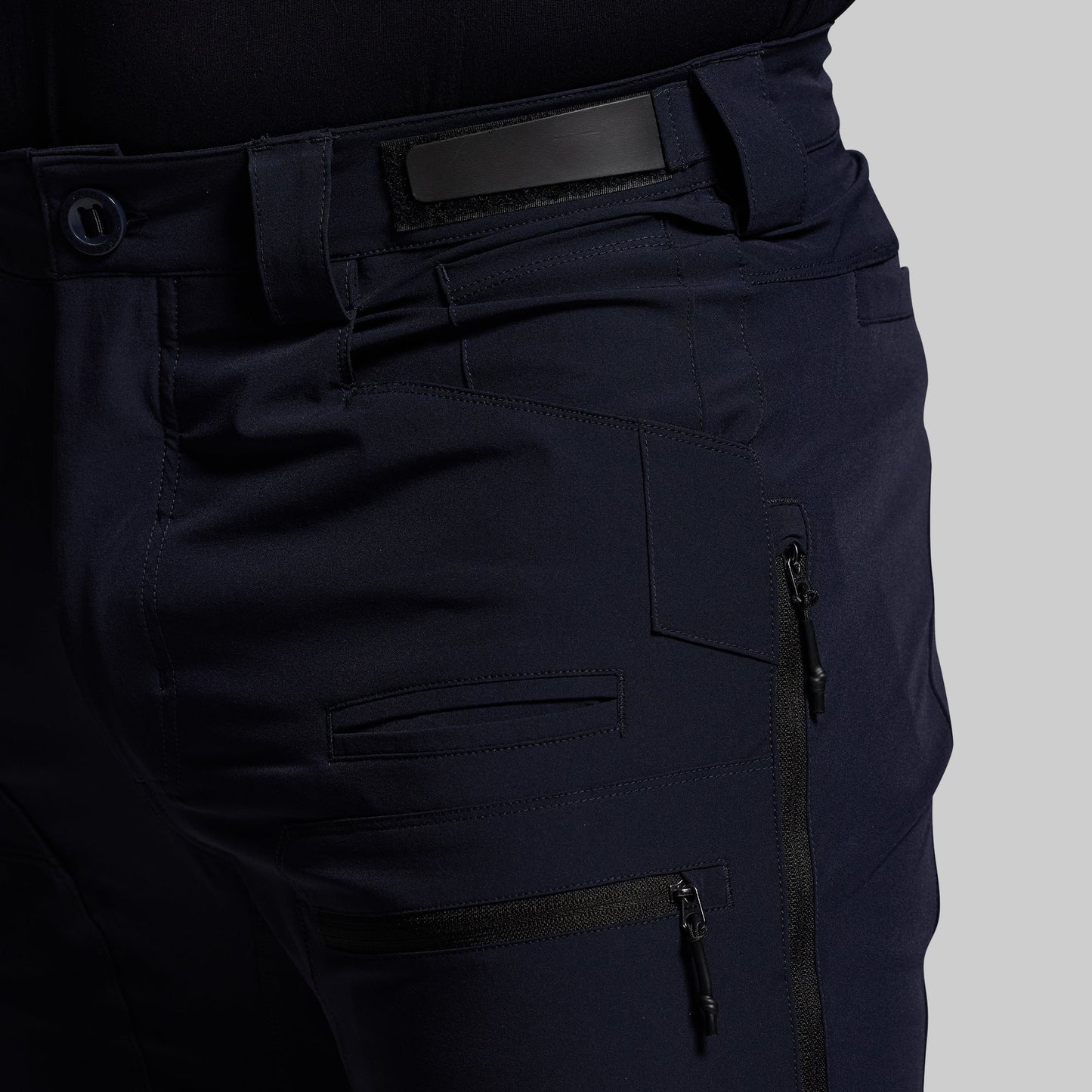 Navy blue outdoor pants with multiple pockets and zippers on a gray background