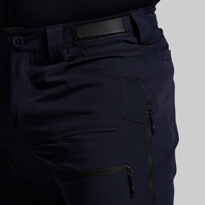 Navy blue outdoor pants with multiple pockets and zippers on a gray background