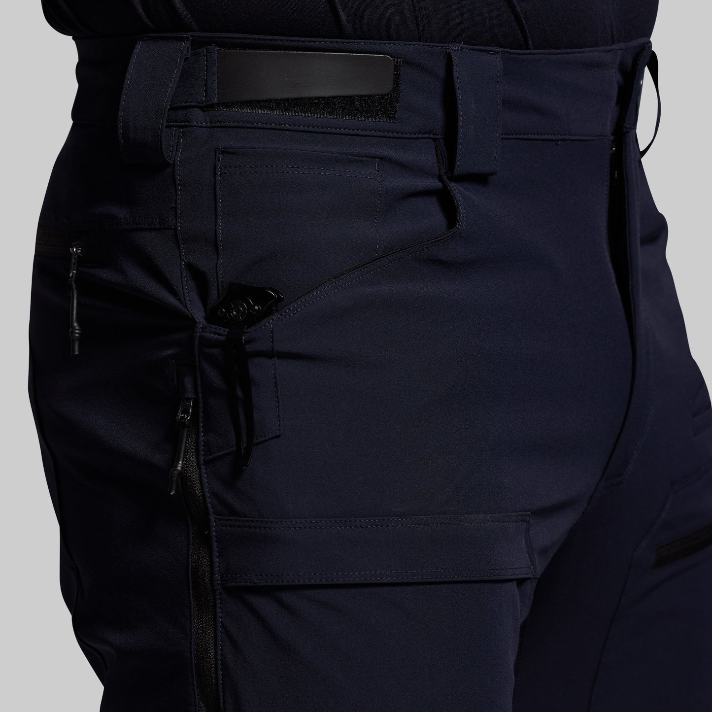 Close-up of dark blue outdoor pants with multiple pockets on a light gray background