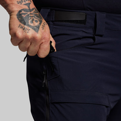 Person wearing dark blue outdoor pants with a tattooed hand on a gray background