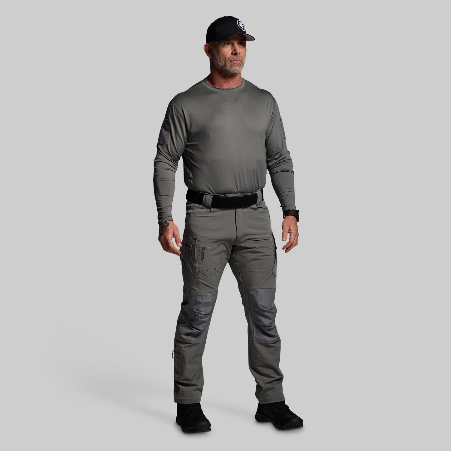 Man wearing a gray long-sleeve shirt and pants with a black cap on a light gray background