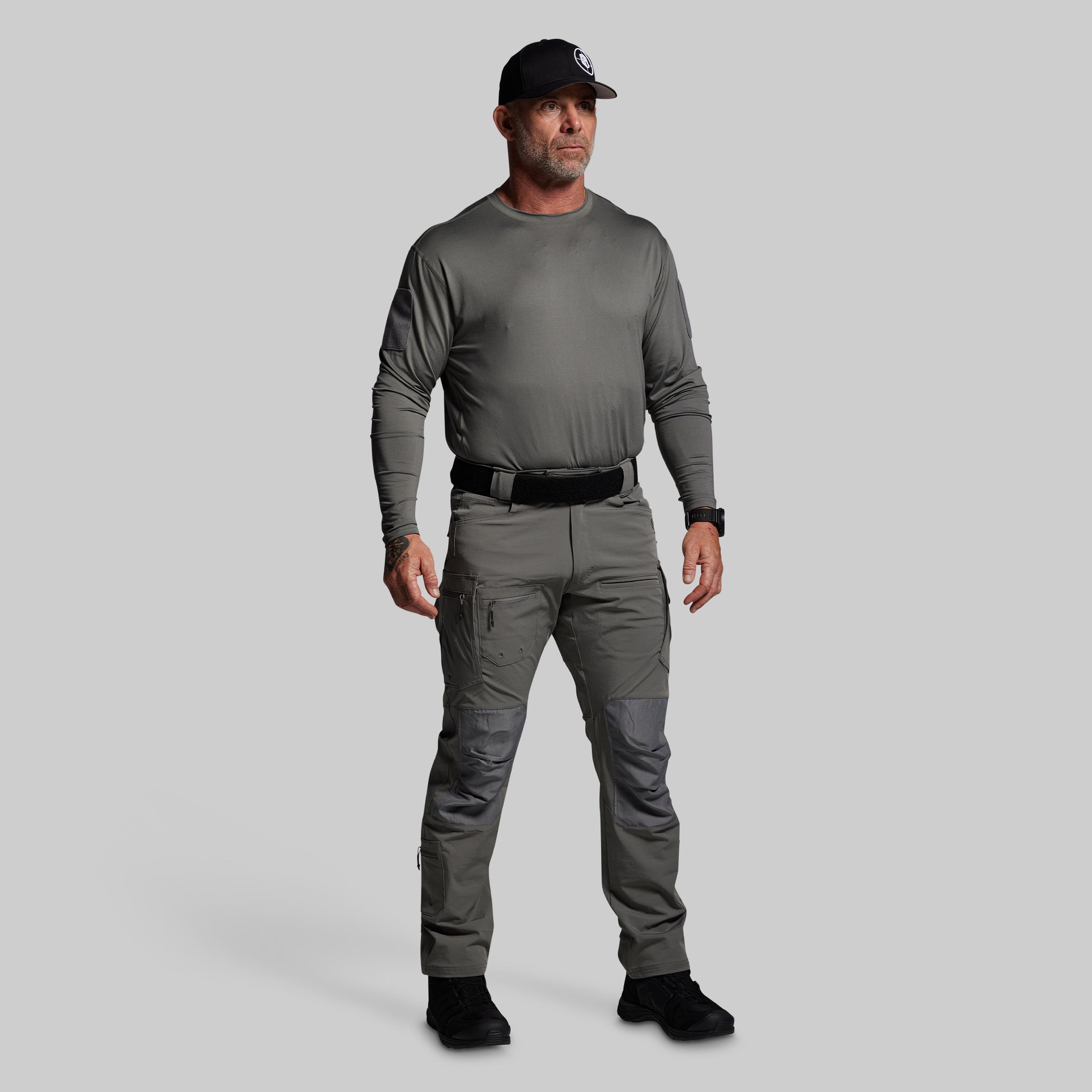 Man wearing a gray long-sleeve shirt and pants with a black cap on a light gray background