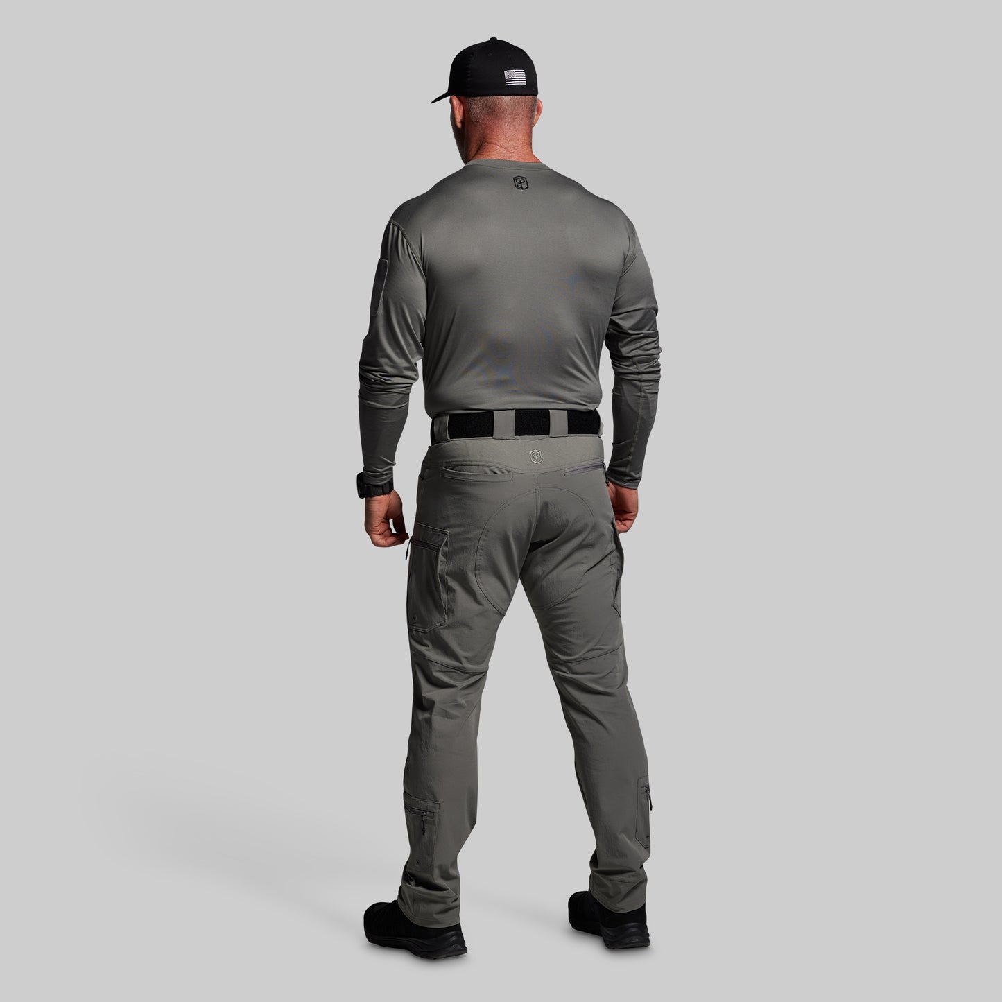 Man wearing a gray long-sleeve shirt and pants with a black cap on a light gray background