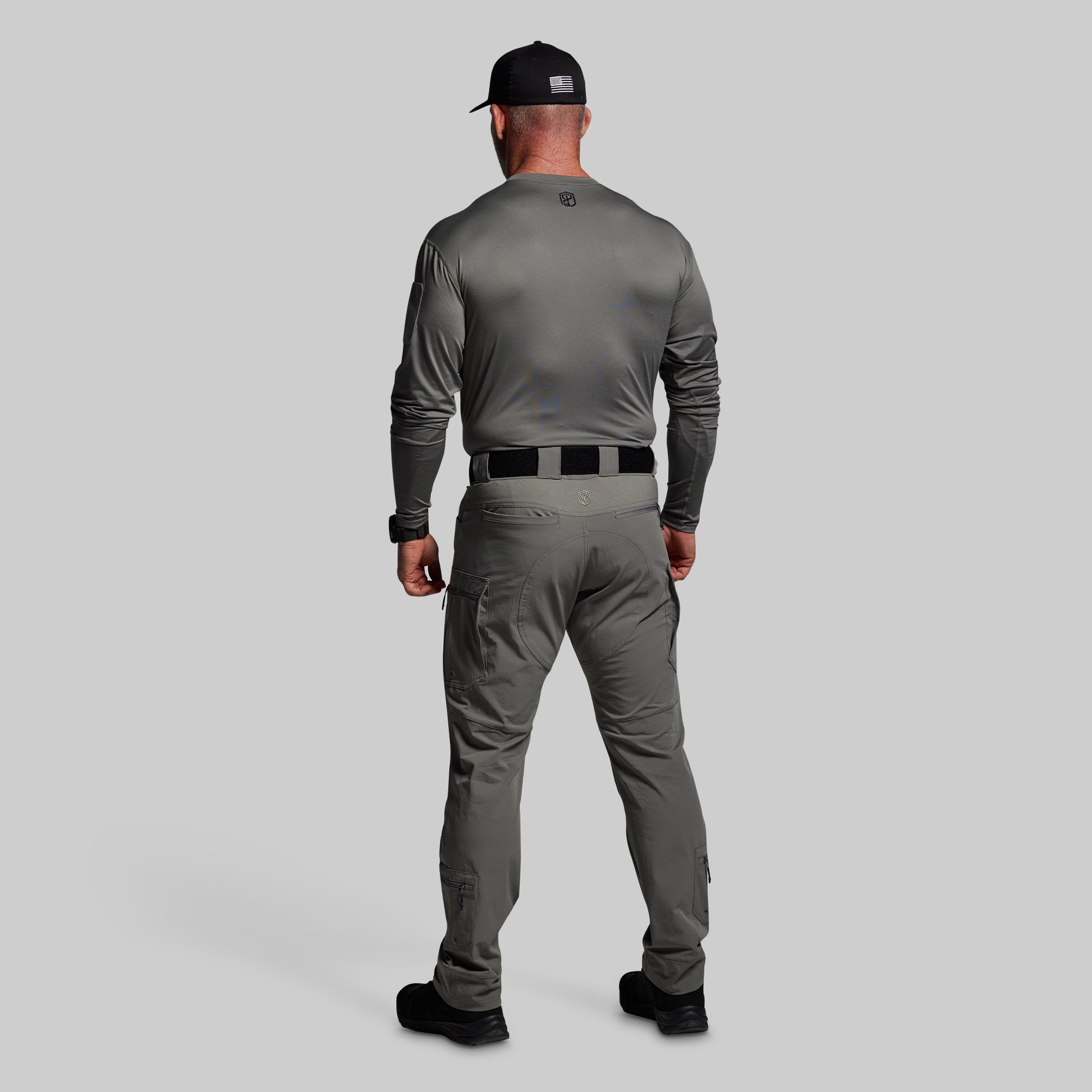 Man wearing a gray long-sleeve shirt and pants with a black cap on a light gray background