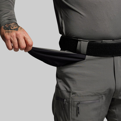 Person wearing dark gray pants with a tattooed arm on a light gray background