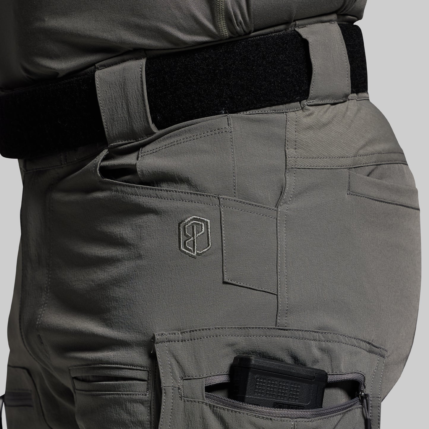 Close-up of tactical pants with a visible brand logo on a gray background