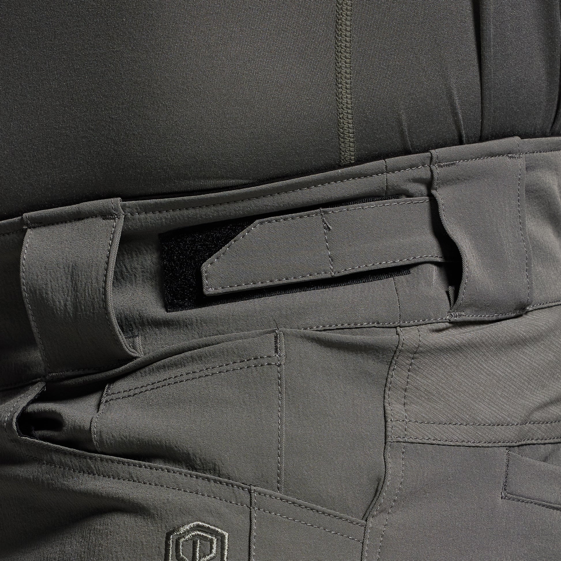 Close-up of gray tactical pants with adjustable waistband and a brand logo.